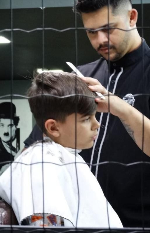 Barbeiro da Menegatti cortando o cabelo de uma criança com atenção